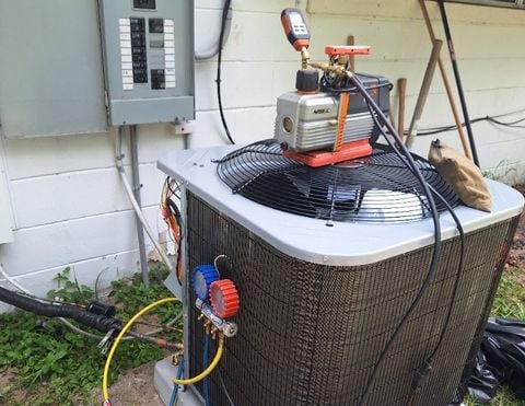 A vacuum pump and gauges on top of an outdoor condenser during an installation