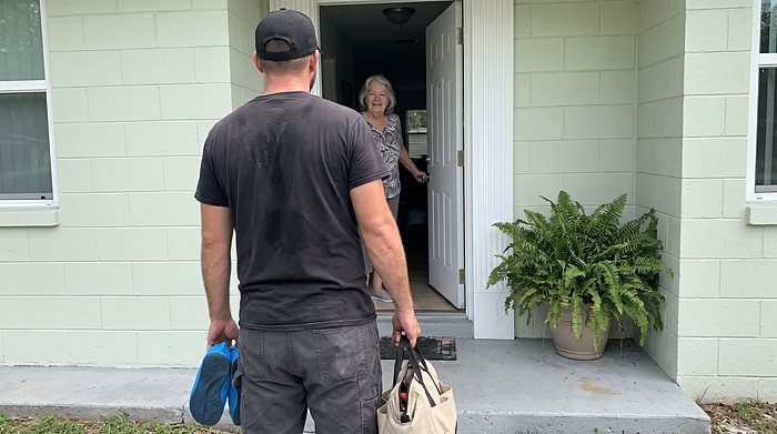 A technician with a tool bag greets a homeowner at the front door