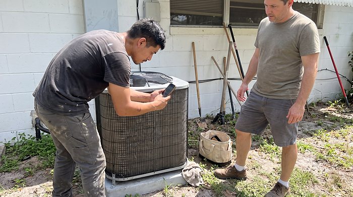 A technician and a homeowner look over a newly set outdoor AC unit