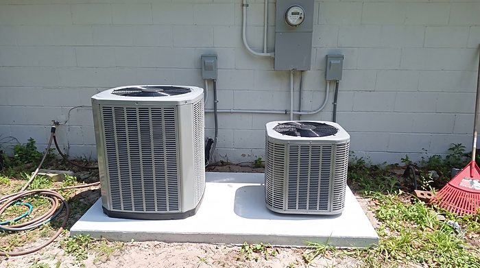 Two new outdoor condensers side by side on a shared concrete pad