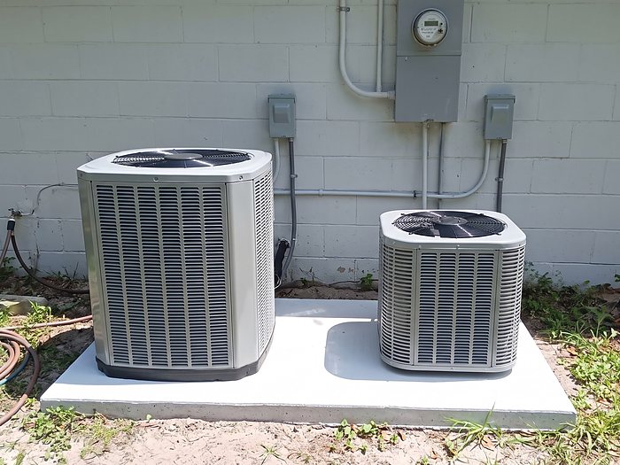 Two new condensers of different sizes sit side by side on a fresh white pad against a gray block wall