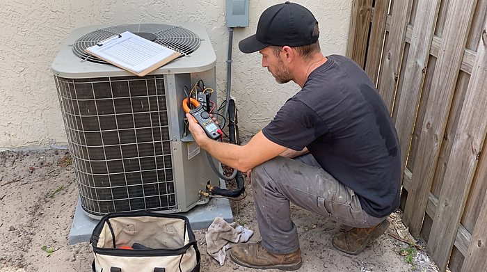 A technician tests the electrical connections on an outdoor condenser with a multimeter