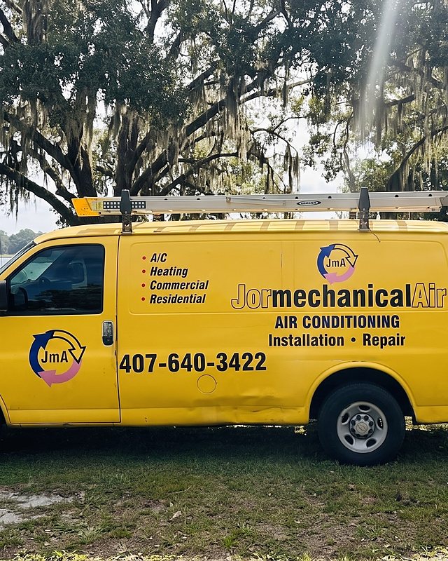 The yellow Jormechanical Air van parked on a grass shoulder by a lake under live oaks draped in Spanish moss