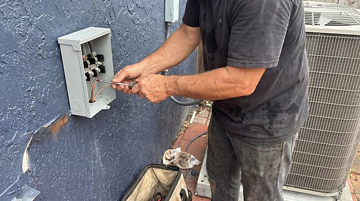 A technician wires an outdoor disconnect box on a stucco wall