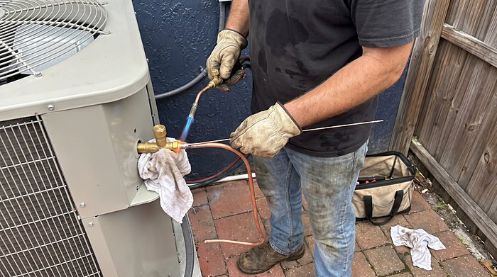 A technician brazes a copper refrigerant line at an outdoor unit