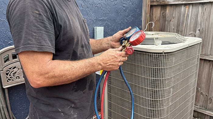 A technician reads refrigerant gauges connected to an outdoor condenser