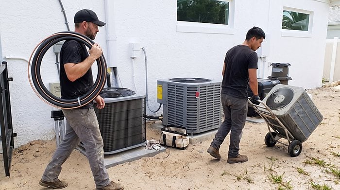 Two technicians move a new condenser into place on install day