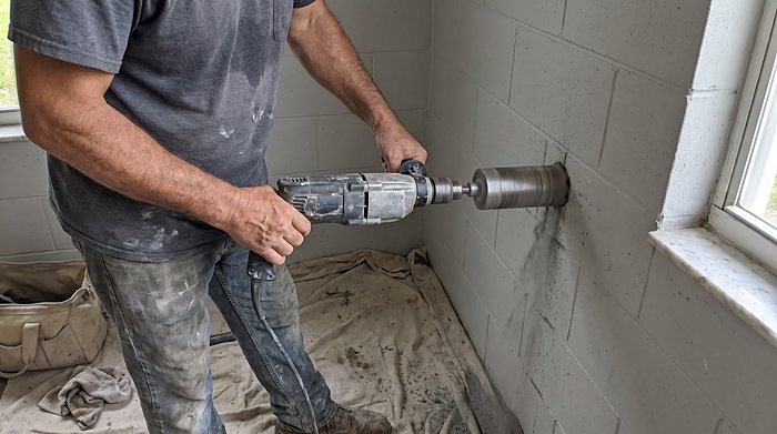 A technician drills through a block wall for a mini-split line set