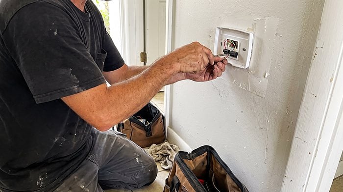 A technician fits a new thermostat to the wall