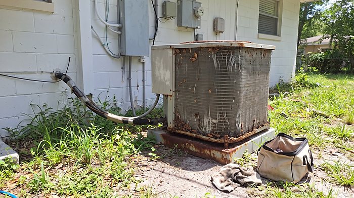 A rusted, failing outdoor unit on a corroded stand beside a Florida home