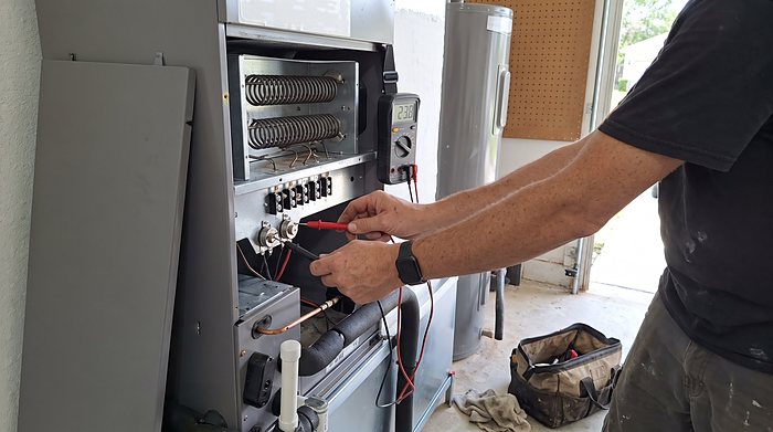A technician tests the heat strip inside an air handler with a meter