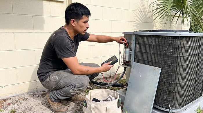 A technician tests an outdoor condenser with a multimeter