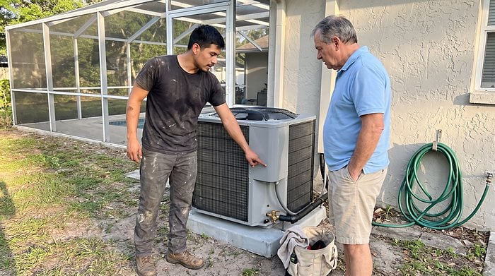 A technician talks with a homeowner beside the outdoor AC unit after a service visit