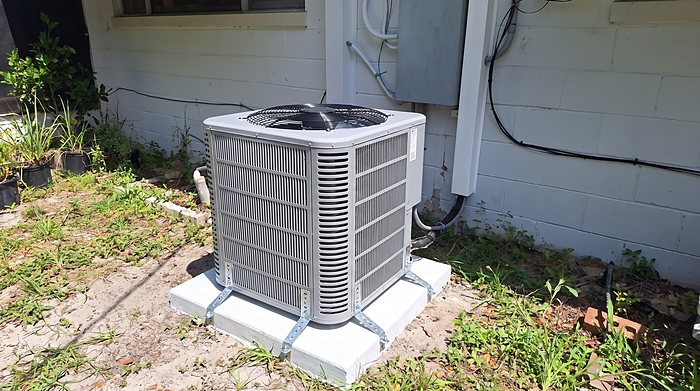 A newly installed heat pump condenser on a pad beside a white block house