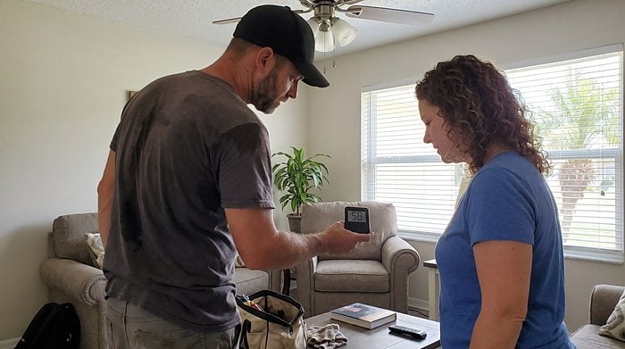 A technician shows a homeowner readings on a handheld air quality meter