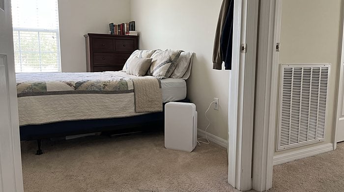 A bedroom with a wall return grille and a portable dehumidifier