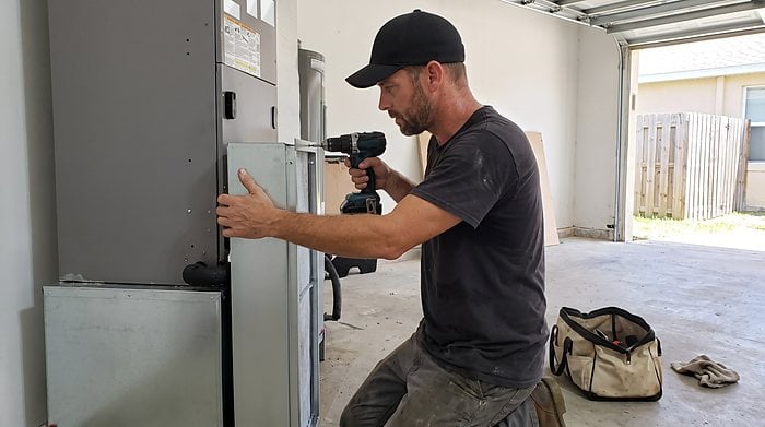 A technician fastens the panel of a garage air handler