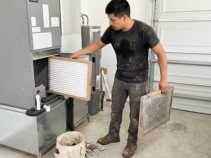 A technician slides a new air filter into a garage air handler while holding the dirty one in his other hand