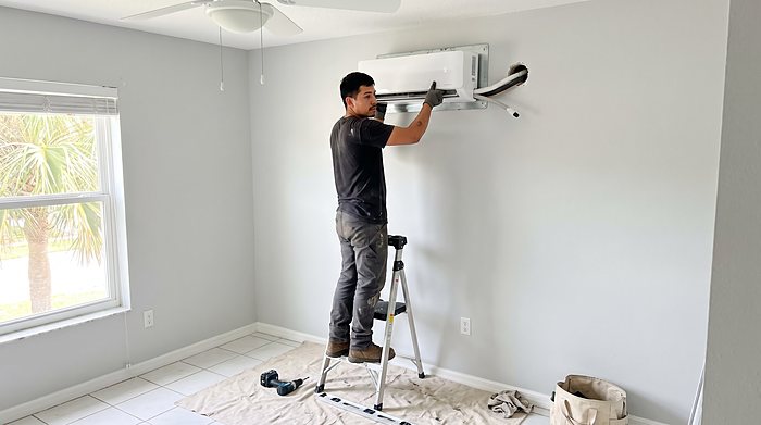 A technician installs a ductless mini-split indoor unit on a bedroom wall