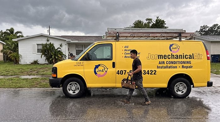 A technician walks to the yellow Jormechanical Air van as storm clouds gather over an Orlando street