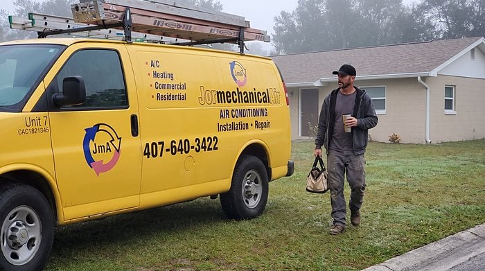 A technician with a tool bag walks from the Jormechanical Air van to a home on a misty morning